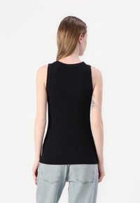 Svart ribbet ermeløs topp med rund hals, tettsittende design og glatt tekstur. Brukt sammen med lyseblå slitte denimjeans.