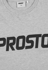 Szara koszulka z bawełny, z dużym czarnym nadrukiem logo "PROSTO" na przodzie. Metka z napisem "LARGE" znajduje się wewnątrz kołnierza.