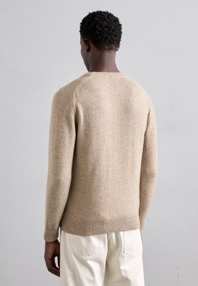Beige gyapjú pulóver ribbed mandzsettákkal és hemel, kerek nyakkivágással és textúrázott felülettel. Hátulról látható, világos nadrággal viselve.