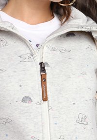 Vaaleanharmaa vetoketjuhuppari, jossa on jääkarhu- ja iglu-kuvioita. Valmistettu pehmeästä kankaasta, jossa on etuvetoketju ja tekstuuri.