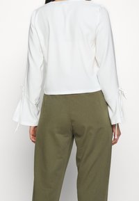 Top bianco corti con maniche a campana, con dettagli legati ai polsini, abbinato a pantaloni verdi oliva a vita alta.