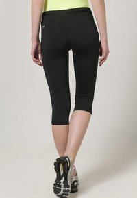 Leggings capri neri in materiale elastico, con una texture liscia, design aderente e una fascia larga in vita.