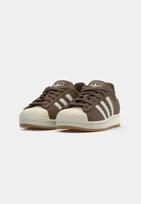 Sneaker in suede marrone con strisce bianche, punta in gomma e suola in gomma. Presenta un collare imbottito e un logo classico sulla linguetta.