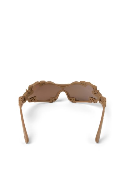 Lunettes de soleil marron avec des bords de monture irréguliers et ondulés, ainsi que des verres teintés marron assortis, sur un fond blanc.