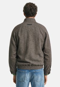 Bruine herringbone-gepatroniseerde jas met een lage kraag, elastische tailleband en knoopmanchetten; gecombineerd met lichtblauwe denim jeans.