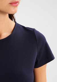 Marinblå t-shirt med kort ärm och rund halsringning, tillverkad av ett slätt, figurnära material, som visar en enkel och strömlinjeformad design.