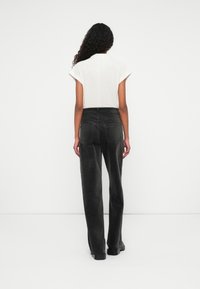 Un haut blanc à manches courtes associé à un jean noir large taille haute. Les jeans comportent des poches arrière et une texture lisse.