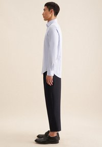 Lichtblauw overhemd met lange mouwen en een puntkraag, gecombineerd met marineblauwe broek en zwarte schoenen, gezien vanaf de zijkant.