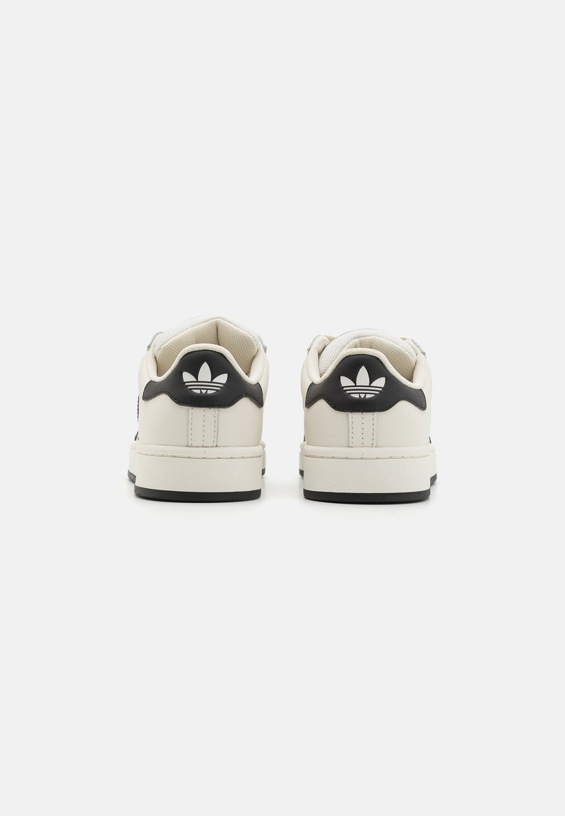 Baskets en cuir blanc avec des accents noirs, talon arrondi, semelle texturée et logo classique à trois bandes sur l'onglet du talon arrière.