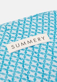 Producto textil con un patrón geométrico en azul y blanco. La etiqueta dice "SUMMERY" en una etiqueta de tela color crema.