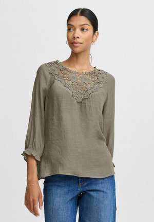 Blusa verde oliva con un colletto in crochet dettagliato, maniche lunghe con polsini a volant e una vestibilità comoda, realizzata in tessuto leggero.