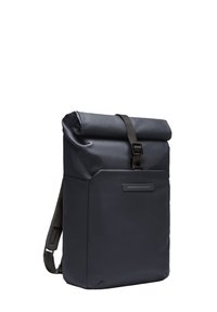 Sac à dos à rabat fabriqué en tissu navy durable, avec une poche avant, une sangle noire réglable, et un design minimaliste élégant.