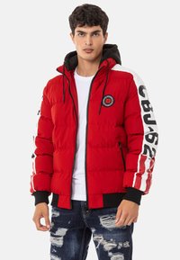 Red puffer jacket with black accents, zipper closure, and logo patch. Features white striped detailing on sleeves and ribbed cuffs.