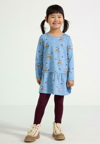Blå langærmet kjole med blomstermønster og hjortetryk, lagdelt kant, parret med burgunder leggings og brune snørebåndsstøvler. Glat stoftekstur.