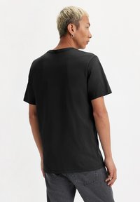Camiseta de algodón negra de manga corta y cuello redondo, con un diseño liso. La tela parece suave y transpirable.