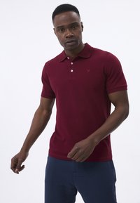 Burgunderfarvet polo shirt med krave, korte �ærmer og tre-knaps lukning; har et lille logo på brystet.