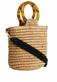 Spleciona torebka ze słomy z dużymi okrągłymi uchwytami w kolorze żółwia i odpinanym szerokim czarnym paskiem na ramię.