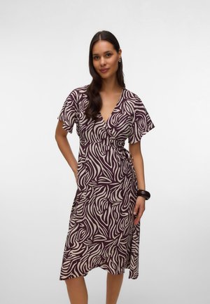 Mujer que lleva un vestido cruzado de manga corta, con escote en V y largo hasta la rodilla, con un estampado abstracto de cebra en tonos púrpura oscuro y beige.