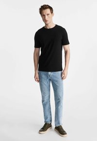 Czarny krótki rękaw t-shirt w połączeniu z jasnoniebieskimi dżinsami i zielonymi trampkami. T-shirt ma okrągły dekolt, prosty design i miękką teksturę.