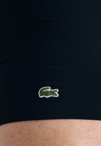 Boxer shorts en coton noir avec un logo de crocodile brodé vert sur la cuisse gauche, texture lisse et coupe ajustée.