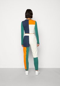 Värgblöckad träningsdräkt i marinblått, grönt, orange och vitt. Har långa ärmar, elastisk midja, muddar på byxorna och en kortad design.