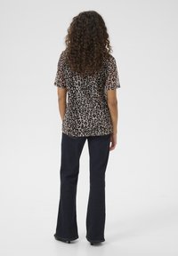 Top corto a maniche corte con stampa leopardata, realizzato in tessuto trasparente; abbinato a jeans svasati blu scuro, con design classico e leggera trama.