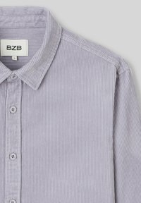 Chemise en velours côtelé violet clair avec un col boutonné, cinq boutons sur le devant et des rainures verticales texturées sur le tissu.