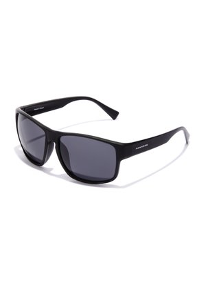 Ochelari de soare negri cu o finisare mată, lentile dreptunghiulare și brațe subțiri. "HAWKERS" este embosat pe lateral.