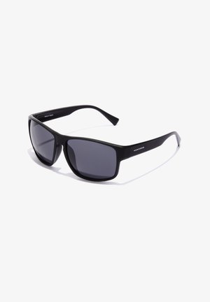 Ochelari de soare negri cu o finisare mată, lentile dreptunghiulare și brațe subțiri. "HAWKERS" este embosat pe lateral.