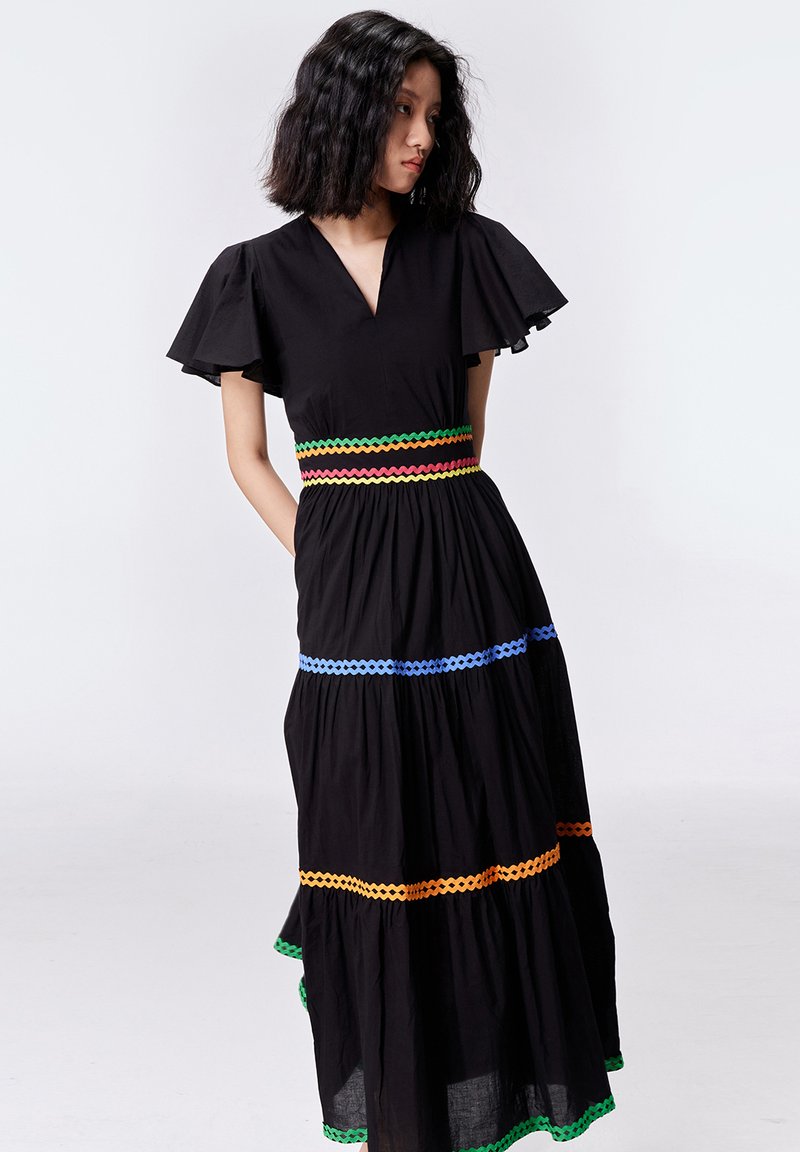 Robe maxi noire avec décolleté en V et manches volantées. Des accents colorés en zigzag contrastant à la taille et une jupe à volants ajoutent du détail.