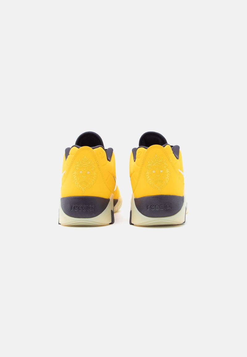 Yellow sneakers with gray accents, featuring a lion emblem and "reactx" branding on the heel. Smooth texture and rounded design.