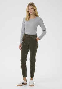 Olivenfarvede kordfløjspants med en slim fit og forlommer, parret med en grå langærmet top og hvide sneakers med sorte detaljer.