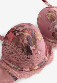 Rožinė paminkštinta liemenėlė su gėlių raštu, nėrinių apdaila ant juostos ir kraštų, prieš baltą foną.