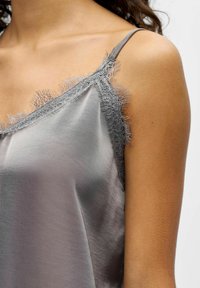 Camisole en satin gris avec bordure en dentelle le long de l'encolure et bretelles spaghetti réglables, présentant une texture lisse et brillante.