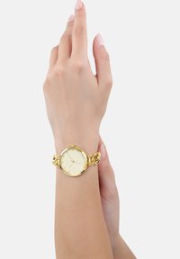 Goldfarbene Armbanduhr mit rundem Zifferblatt und verlinktem Armbanddesign. Das Zifferblatt weist goldene Markierungen und eine glatte, glänzende Oberfläche auf.