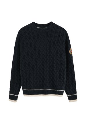 Pull en maille torsadée bleu marine avec un col rond côtelé, ourlet et poignets rayés beige clair et blanc, présentant un patch logo sur la manche.