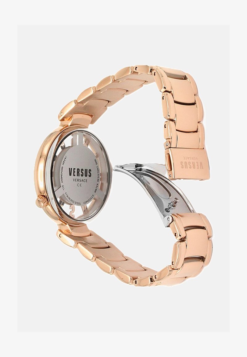 Kuldtooniline roostevaba terasest kell, millel on ümmargune korpus, hõbedane kellapäev ja link-ristmik. Omab klambri sulgemist ja julgeid numbreid.