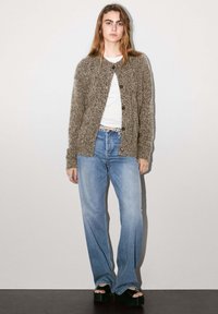 Grå texturerad cardigan med rund hals, knäppning, som bärs över en vit t-shirt; ihop med ljusblå utsvängda jeans och svarta platåsandaler.
