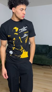 Melnā kokvilnas T-krekls ar dzelteniem grafiskiem uzrakstiem un attēliem, apaļu kaklu, īsām piedurknēm, kombinēts ar melnām biksēm ar tekstūru.