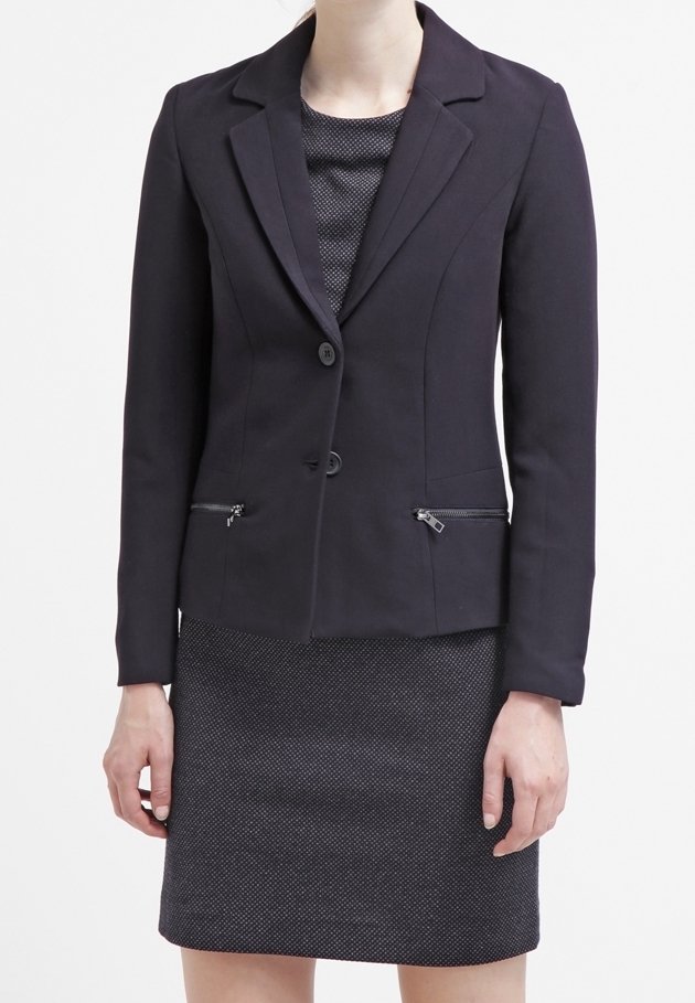 Granatowa marynarka z klapami, dwoma guzikami i zamykanymi kieszeniami. Noszona na tle strukturalnej, ciemnoszarej sukienki. Dopasowany krój i gładki materiał.