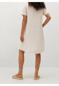 Vestido de manga corta, de color beige pálido, con corte recto, textura suave y detalle en la costura trasera, combinado con sandalias de tiras color beige claro.