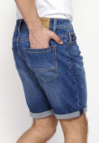 Shorts de denim en un lavado azul medio con dobladillos enrollados. Presenta cinco bolsillos, costuras en contraste y un parche de cuero con la marca en la cinturilla.