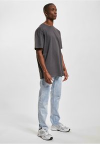 Pilkas medvilnės marškinėliai trumpomis rankovėmis derinami su šviesiai mėlynomis džinsinėmis kelnėmis. Modelis dėvi baltus ir pilkus sportinius batelius. Paprastas, kasdienis apranga.