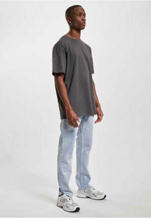 Grå bomull T-skjorte med rund hals, sammen med lyseblå denimjeans. Modellen har på seg hvite og grå sneakers, og står mot en ensfarget bakgrunn.