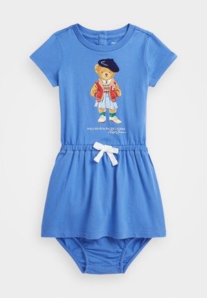 Robe bébé bleue à manches courtes avec taille élastique, nœud blanc, protection de couche attachée et dessin d’un ourson portant une veste et un béret sur le devant.