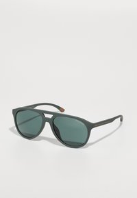 Ochelari de soare din plastic verde, cu o formă unghiulară distinctă, lentile întunecate și accente portocalii pe braț, prezentând un design minimalist.