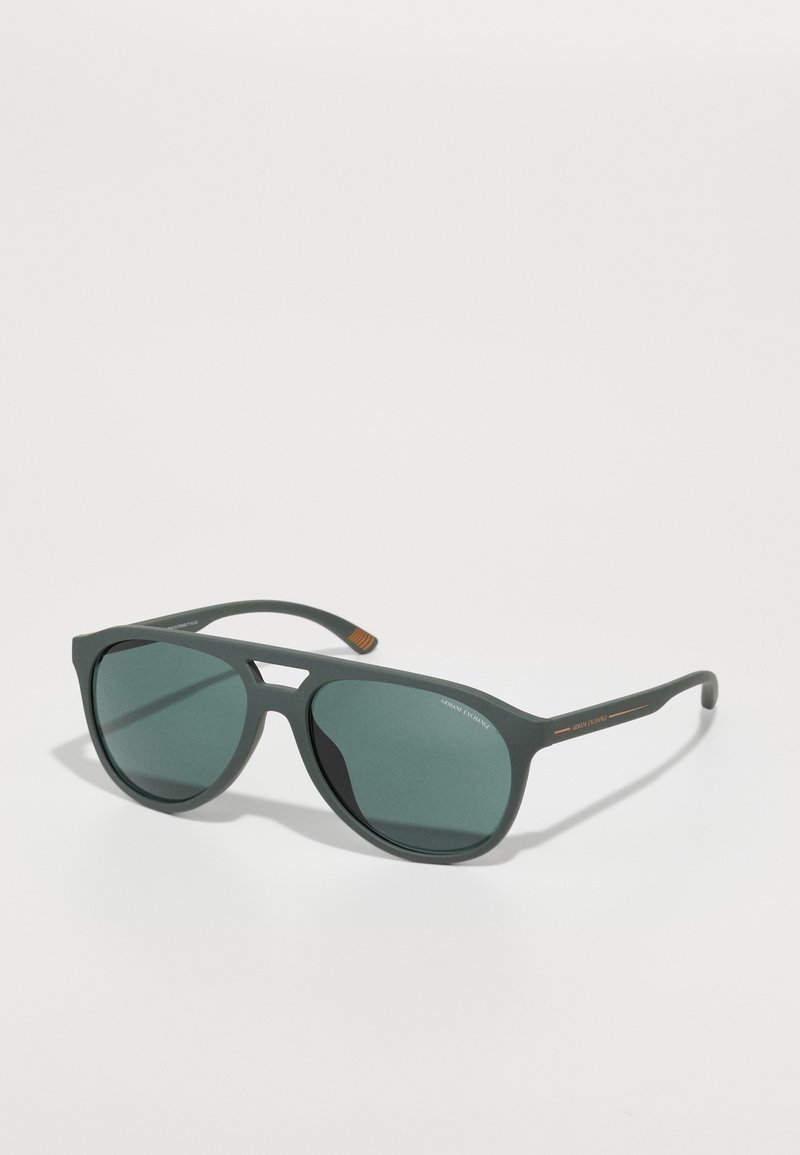 Ochelari de soare din plastic verde, cu o formă unghiulară distinctă, lentile întunecate și accente portocalii pe braț, prezentând un design minimalist.