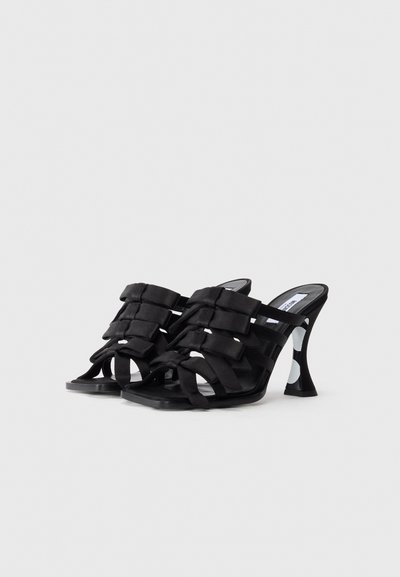 Mules à talons hauts noirs avec de larges sangles croisées rembourrées et un talon évasé noir et blanc à pois.