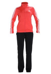 Veste de sport rouge avec fermeture éclair, bandes blanches sur les manches et pantalon noir à jambes droites, présentés sur fond blanc.