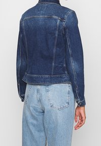 Jeansjacka i mörkblått med en figursydd design, som har en klassisk krage, långa ärmar och subtila sömnadsdetaljer.